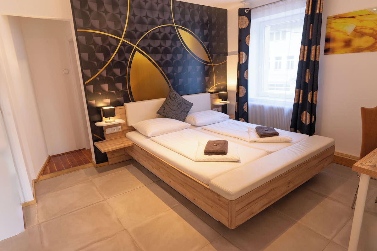 Quarto moderno com cama de madeira, mesas de cabeceira e parede com padrões geométricos.