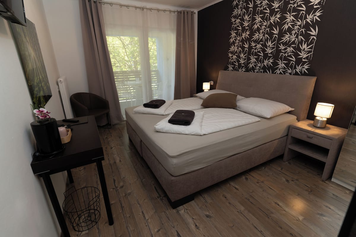 Quarto de hotel moderno com uma cama grande, mesas de cabeceira, escrivaninha e vista para o exterior.