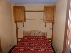 Ein Schlafzimmer mit einem hölzernen Kopfteil, einer roten, gemusterten Bettdecke und Holzschränken über dem Bett.