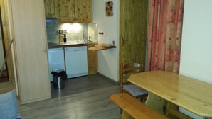 Ett kompakt kök med träskåp, en diskho och en liten diskmaskin. I matplatsen finns ett träbord och en träbänk.