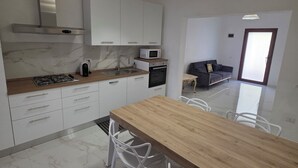 A modern kitchen with white cabinets, a wooden countertop, and a marble backsplash. There is a dining area with a wooden table and white chairs.