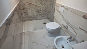 A bathroom with a marble floor, a toilet, a bidet, and a sink.
