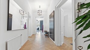 Un couloir avec un plancher en bois, des murs blancs et un grand miroir sur le côté gauche. Il y a une porte sur la droite et une plante au premier plan.