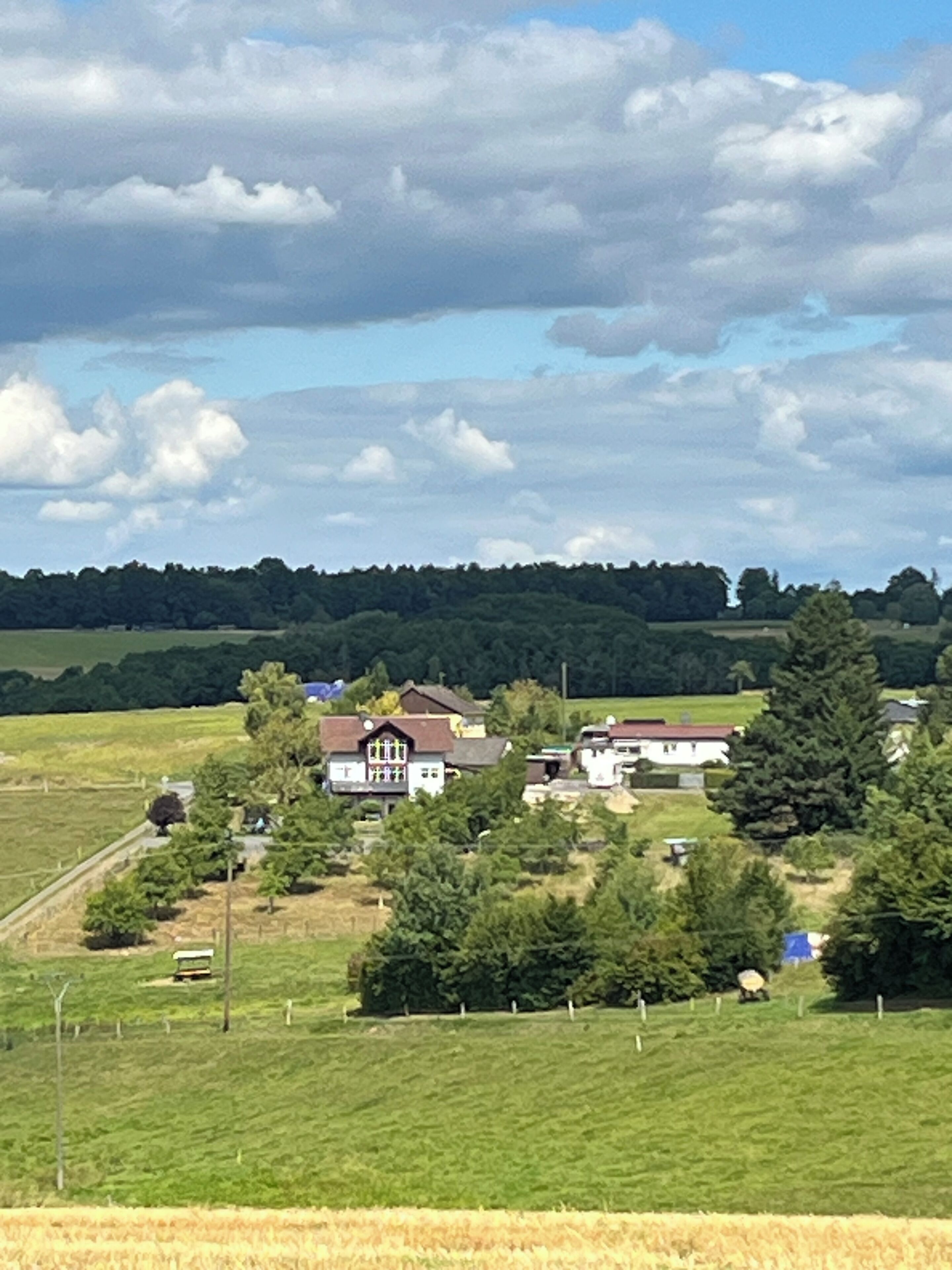 A rural landscape with a cluster of houses surrounded by greenery and fields.