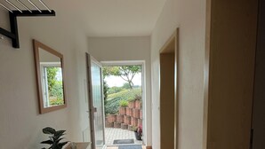 A hallway with a tiled floor, a potted plant, a mirror, and a door leading to an outdoor area with a brick wall and greenery. - Cozy vacation apartment in the green Westerwald, gladly with dogs (Rodenbach bei Puderbach)