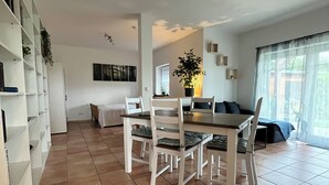 A spacious living area with a dining table and chairs, a bookshelf, and a large window with curtains. - Cozy vacation apartment in the green Westerwald, gladly with dogs (Rodenbach bei Puderbach)
