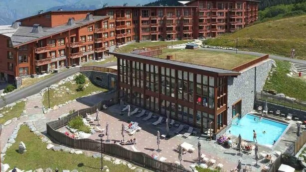 A hotel with a pool area, multiple balconies, and a mountainous backdrop.