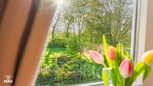 A window view of a garden with a swing set and tulips in the foreground. - Holiday Farm Mau - House 1 (Fehmarn)