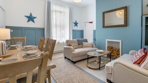 A cozy living room with a dining area, featuring a sofa, coffee table, and a fireplace.