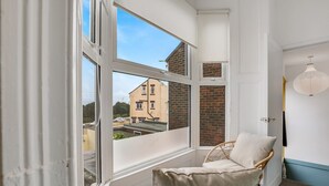 A corner room with a wicker chair, a view of a building through large windows, and a door with a light fixture.
