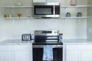 Uma cozinha com micro-ondas, torradeira, forno e uma estante com objetos decorativos.