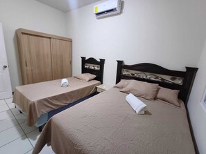 A room with two beds, a wardrobe, and an air conditioning unit.
