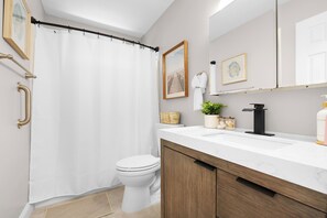 Ein modernes Badezimmer mit weißer Duschvorhang, weißer Toilette, einem Holzwaschtisch mit Marmorplatte, einem schwarzen Wasserhahn und gerahmten Bildern an der Wand.