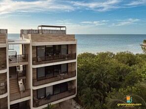 A multi-story building with balconies overlooking a body of water, surrounded by greenery.