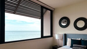 Een slaapkamer met een groot raam, een bed met beddengoed met een patroon, een bedlampje en twee ronde spiegels aan de muur.