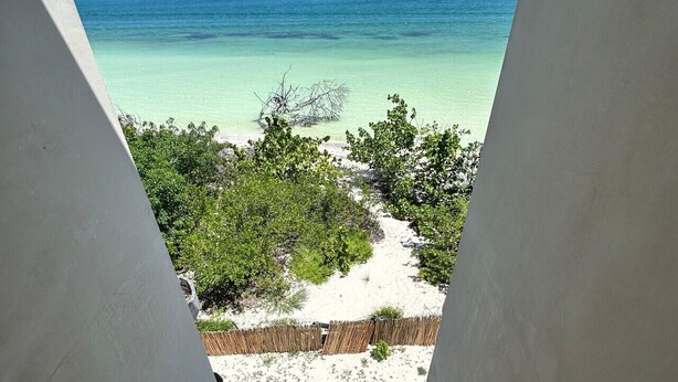 Uitzicht vanaf een balkon op een strand met helder turquoise water en een zandstrand.