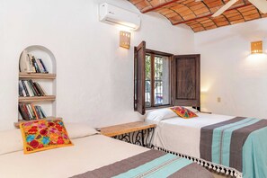 Una habitación con dos camas, una estantería, una ventana con vistas y un aire acondicionado.
