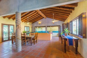A spacious interior with a high ceiling, wooden beams, a dining area, and a kitchen with large windows.