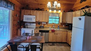 A wooden cabin kitchen with a dining table, chairs, a refrigerator, and a microwave.