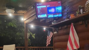 A hot tub area with a television displaying a TV guide, surrounded by wooden walls and a flag.