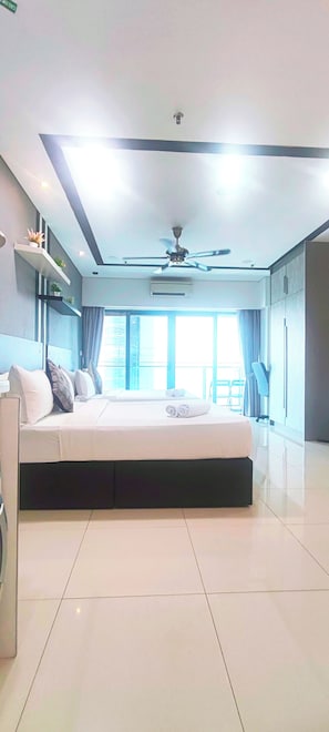 Une chambre à coucher moderne, dotée d’un grand lit, d’un ventilateur de plafond et offrant une vue sur l’extérieur grâce à de grandes fenêtres.
