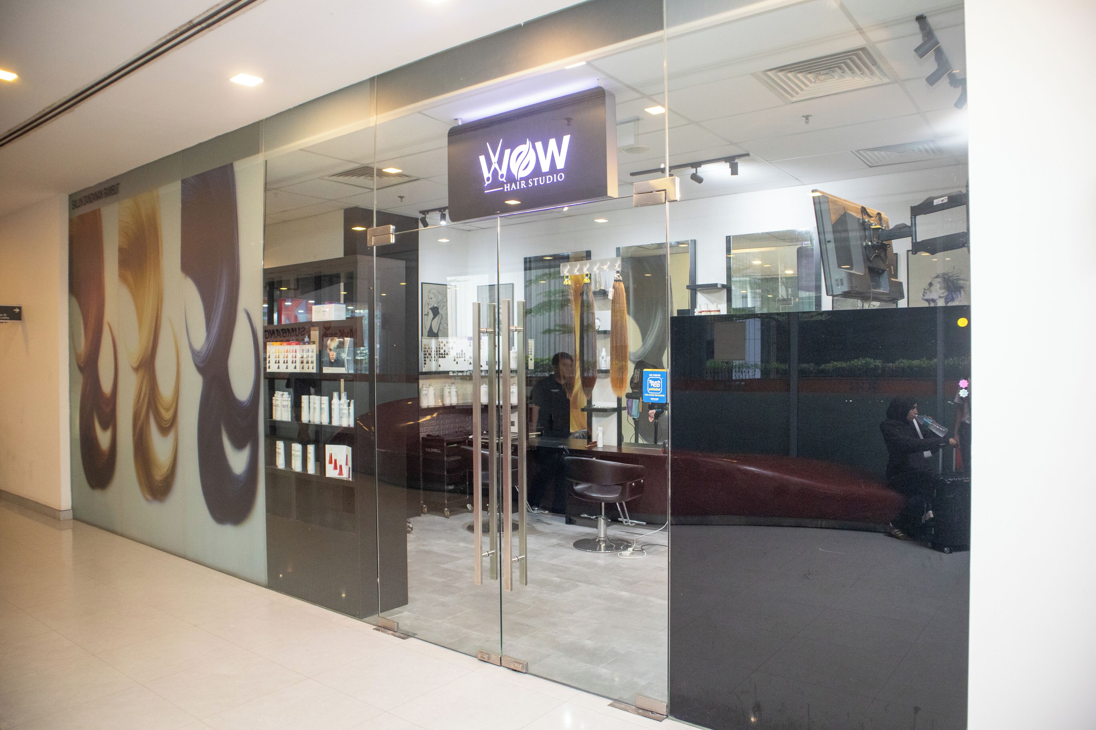 Un salone di parrucchiere con facciata in vetro e interni ben visibili, tra cui una reception e poltrone da parrucchiere.