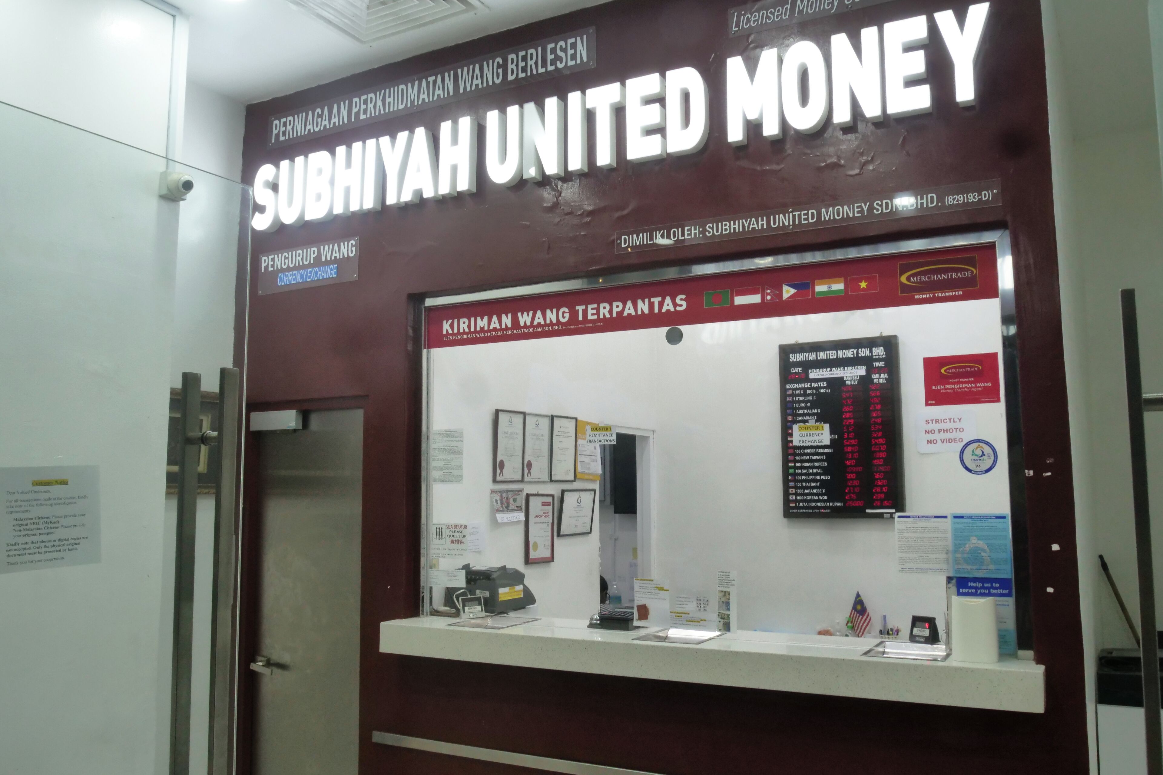 A Subiyah United Money exchange booth with a glass display, currency exchange rates, and various informational posters.