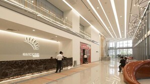 Een moderne hotellobby met een receptiebalie, een glazen lift en een grote, gebogen sculptuur.