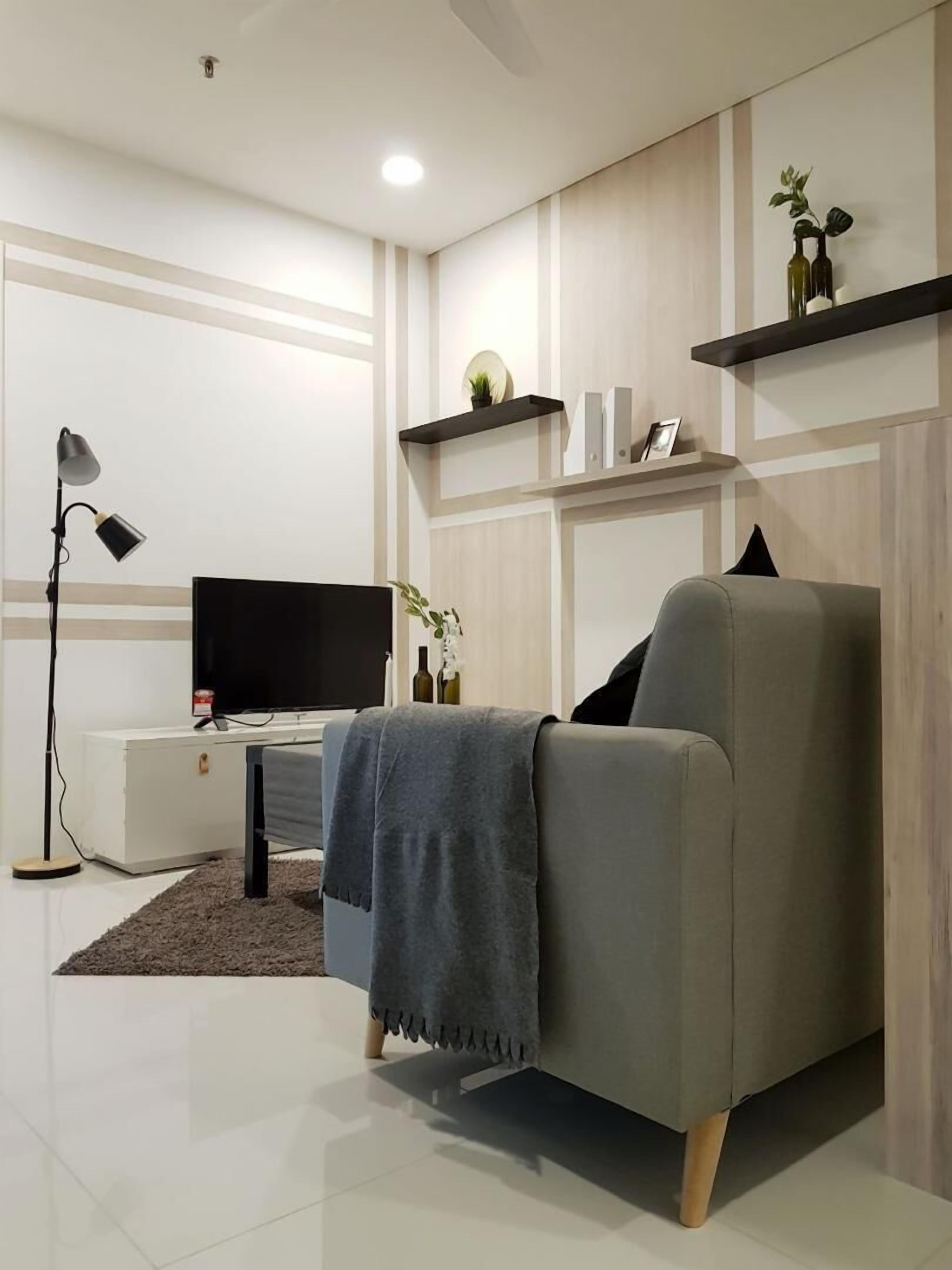 Un soggiorno moderno con un divano grigio, una TV a schermo piatto, una lampada da terra e pareti rivestite in legno.
