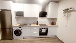 A compact kitchen with a washing machine, a microwave, a toaster, and a small sink.