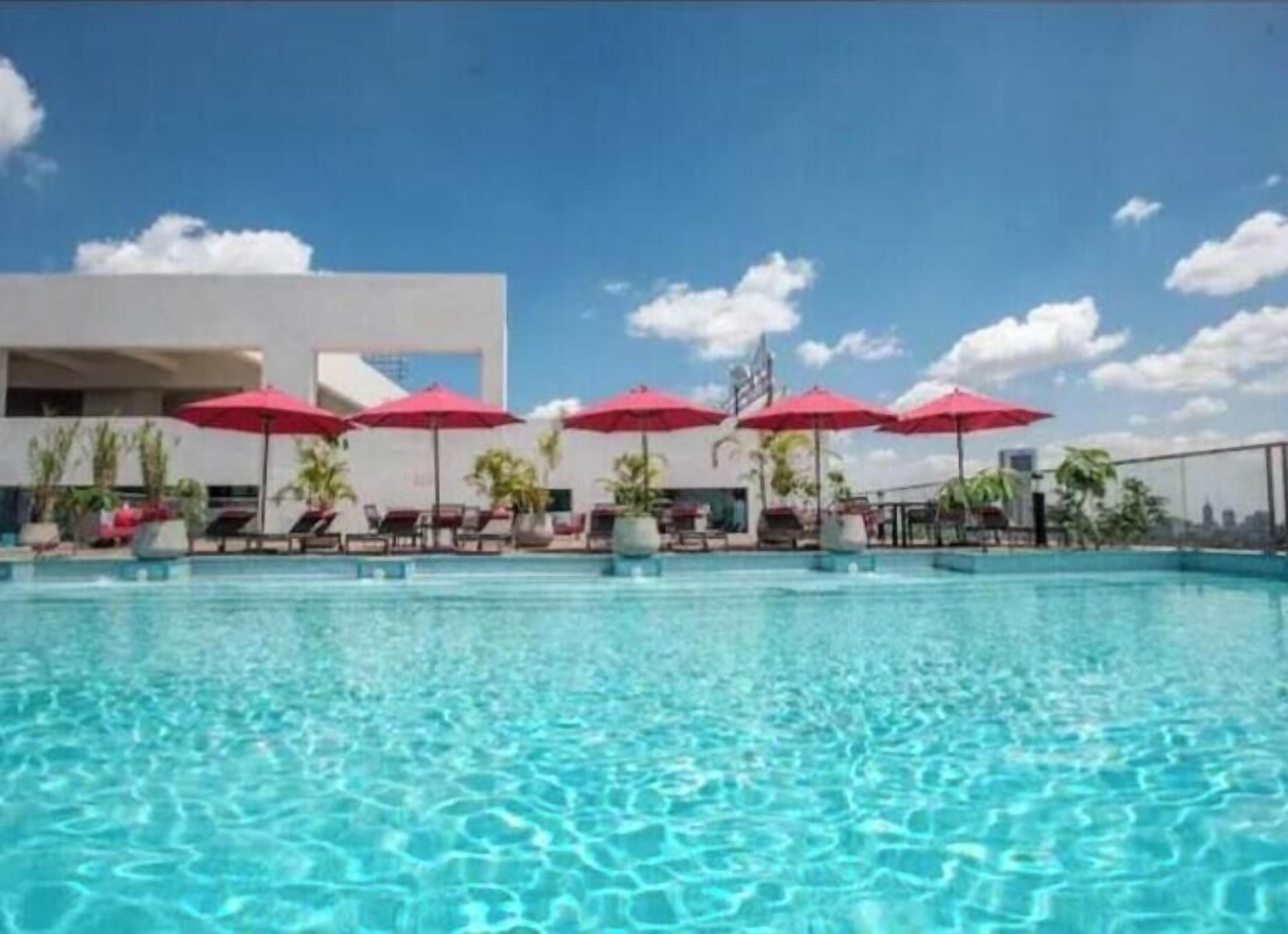 A swimming pool with clear water, surrounded by lounge chairs and red umbrellas.