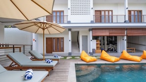 A pool area with lounge chairs and orange bean bags, a staircase, and a view of the building's exterior. - TheNomad Canggu – Modern Deluxe Work Friendly Room in Bali with Pool, Gym & Spa (Bali)