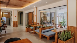 A modern restaurant interior with wooden furniture, green cushioned seating, and potted plants. - TheNomad Canggu – Modern Deluxe Work Friendly Room in Bali with Pool, Gym & Spa (Bali)