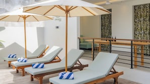 A rooftop lounge area with sun loungers, umbrellas, and a bar. - TheNomad Canggu – Modern Deluxe Work Friendly Room in Bali with Pool, Gym & Spa (Bali)