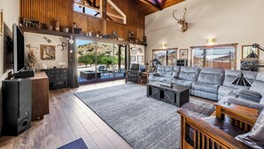 A spacious living room with a large gray sectional sofa, wooden coffee table, and a mounted deer head on the wall.