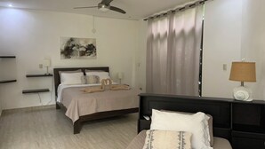 A bedroom with a bed, bedside tables, a ceiling fan, a window with curtains, and artwork on the wall.