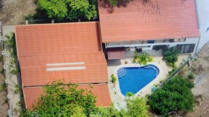An aerial view of a property with a swimming pool, a red-roofed building, and surrounding greenery.