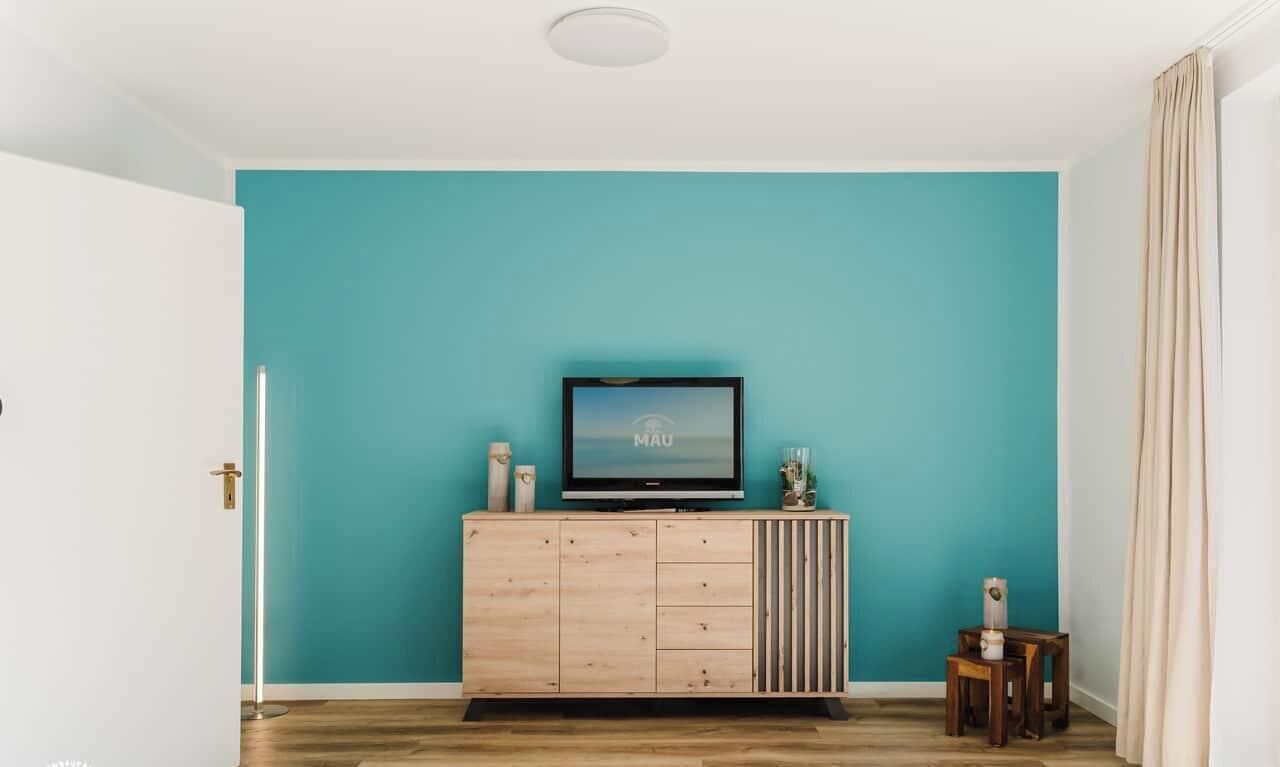 A room with teal walls, a wooden cabinet with a TV, and a small table with a lamp.