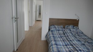 A bedroom with a wooden headboard, a plaid bedspread, and a hallway leading to another room.