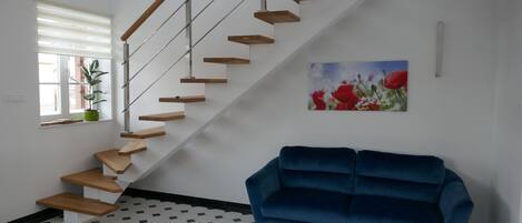 Una escalera con escalones de madera y barandillas de metal, un sofá azul y un cuadro de flores rojas en la pared.