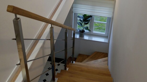 A wooden staircase with a handrail, a window with a view of greenery, and a light fixture above the window.