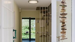 Um corredor com piso de madeira, uma porta de vidro com um suporte de metal e vista para área externa com vegetação.