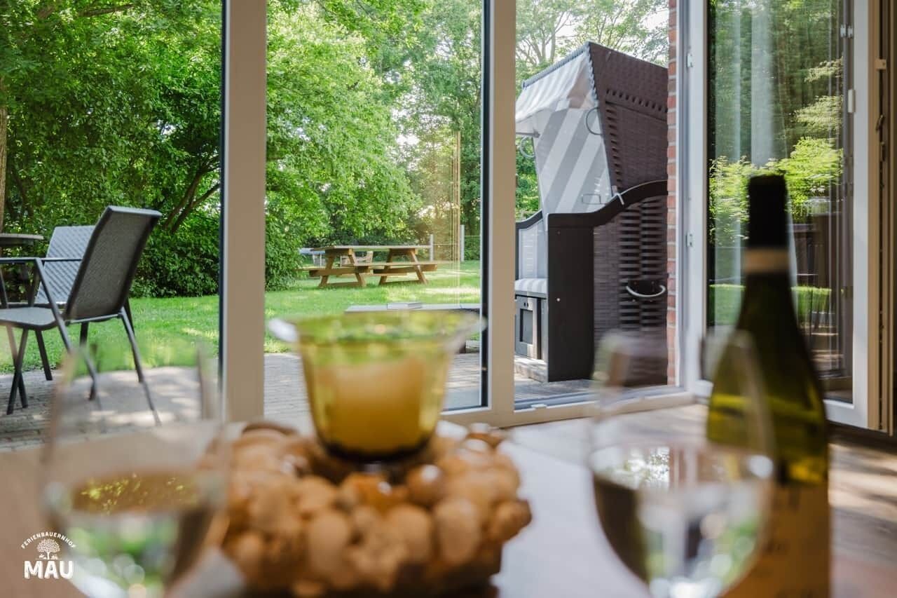 Un espace repas comprenant une table, des chaises et donnant sur un jardin, avec en outre un coin salon extérieur.