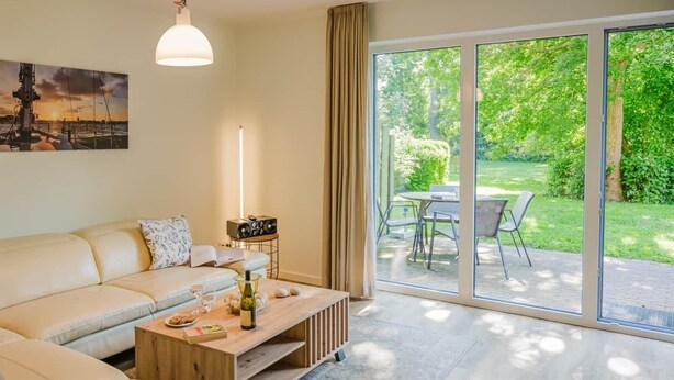 Uma sala de estar moderna com um sofá, mesa de centro e vista para um jardim através de grandes portas de vidro deslizantes.