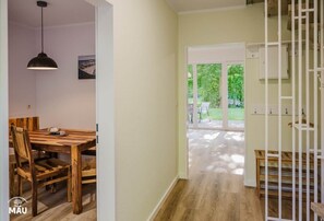 Un pasillo con una mesa de comedor de madera y sillas, una lámpara colgante y vista a un jardín a través de una puerta de cristal.