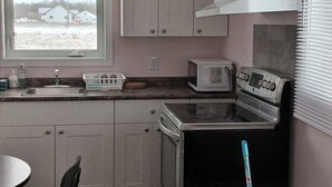 A compact kitchen with a window, a sink, a microwave, and a stove. - Sarah Cottage - 226 Cottage Road, Steeprock , Manitoba (Grahamdale)