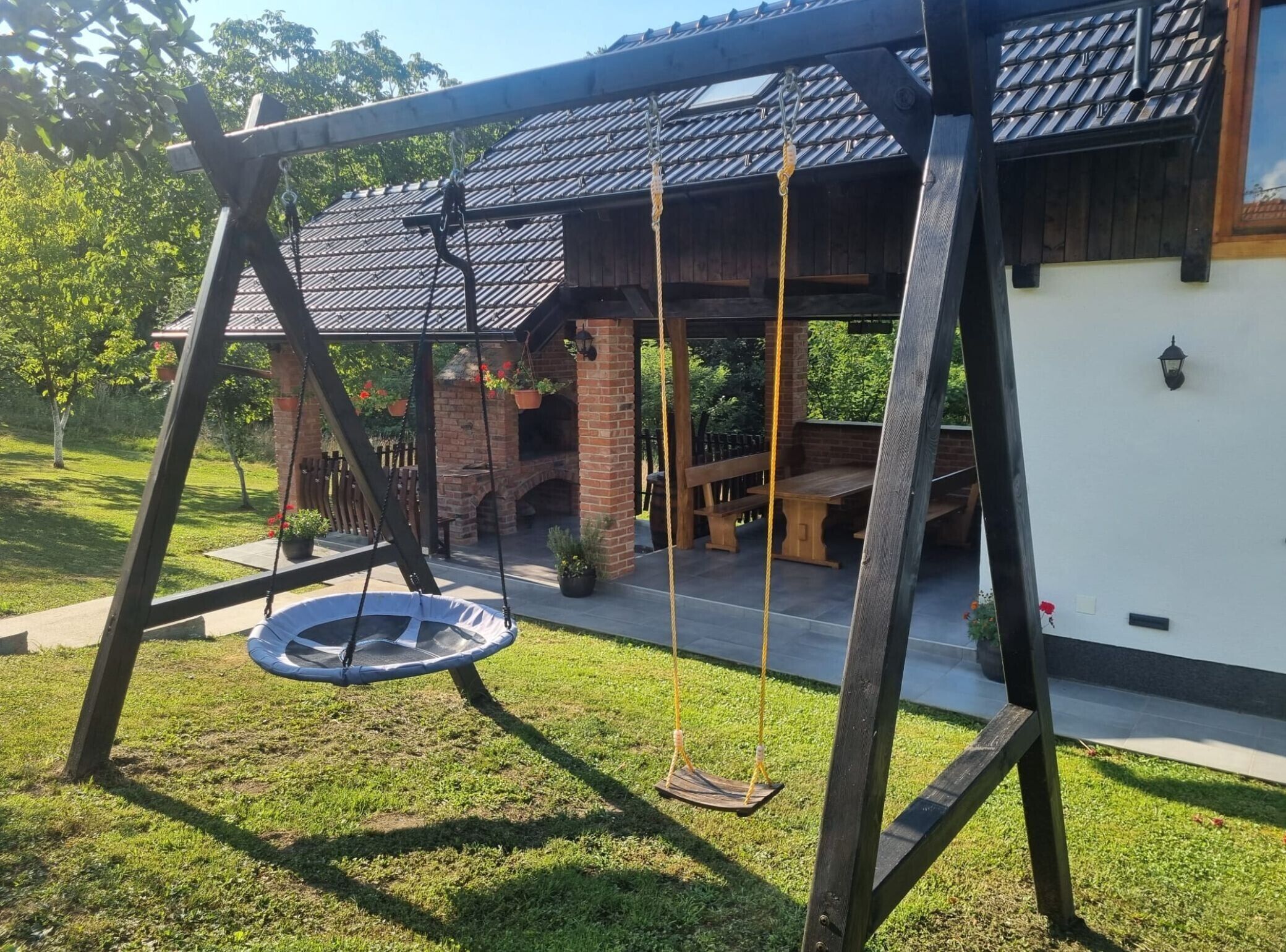 Un’altalena in legno con un trampolino, un’area barbecue in mattoni e un portico coperto con una panchina.