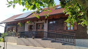Une maison rustique en bois, dotée d’une façade en pierre, d’un balcon avec une rambarde en métal et d’un toit recouvert de tuiles rouges.