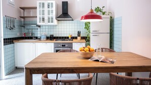 A kitchen with white cabinets, a wooden table, wicker chairs, a red pendant light, and a bowl of fruit. - TrasteverHome -Cisterna Secrets at the Heart of Trastevere (Rome)