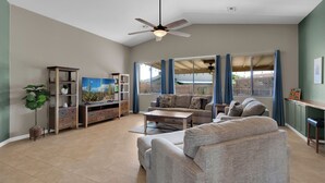 A spacious living room with a ceiling fan, a large window with curtains, a wooden entertainment unit, and a grey sofa. - Beautiful 4-bedroom house with Pool in Tucson (Tucson)